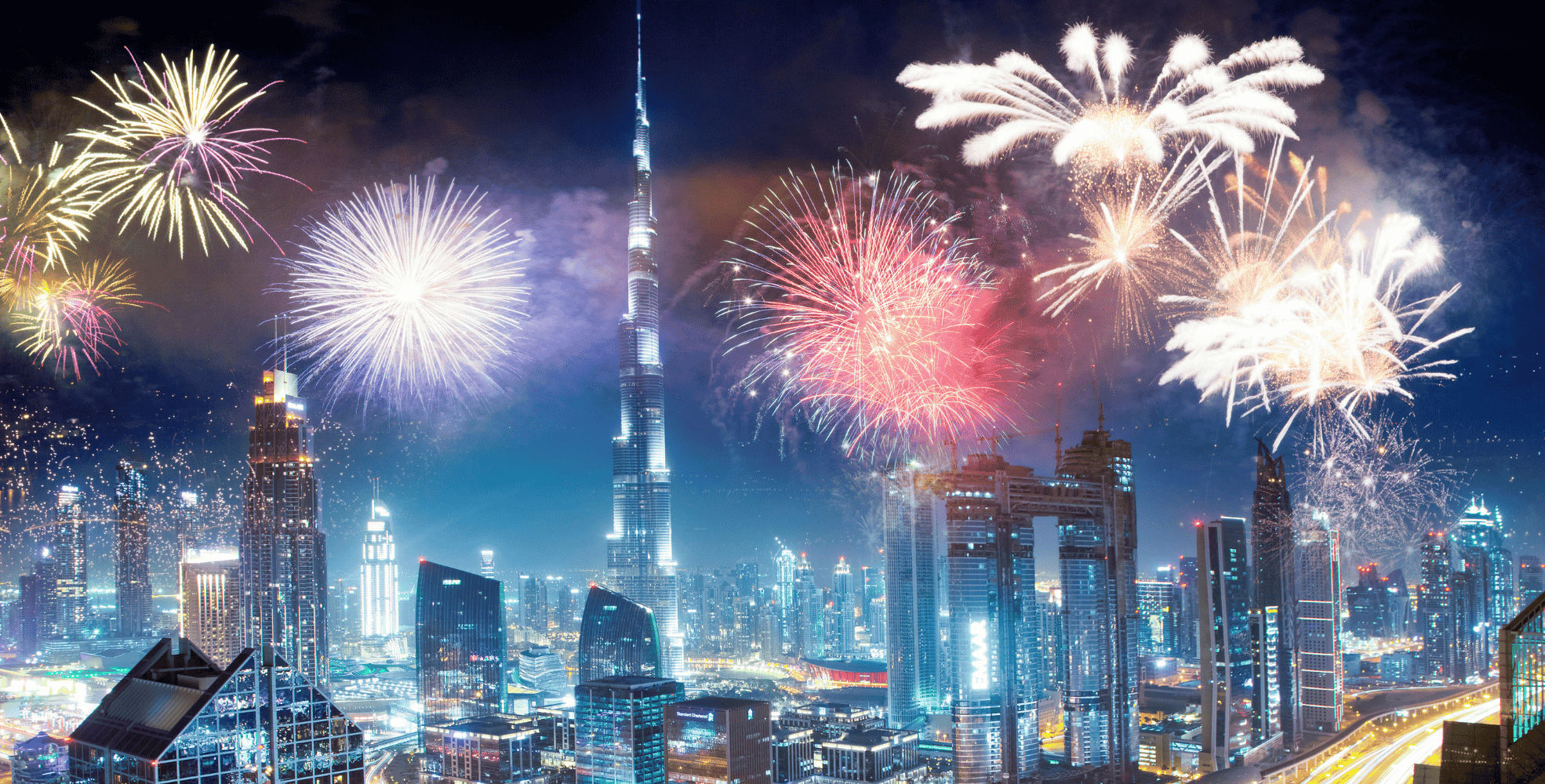Fireworks light up the night sky over a modern city skyline with tall skyscrapers and illuminated buildings.