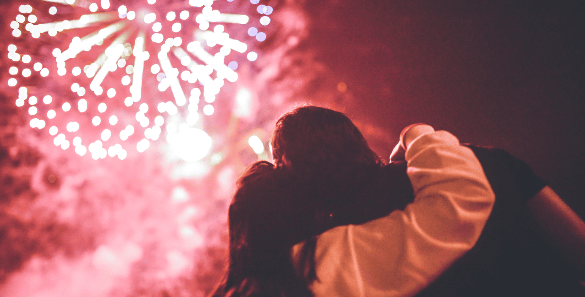 Two people with their arms around each other watch colorful fireworks light up the night sky, celebrating Chinese New Year.